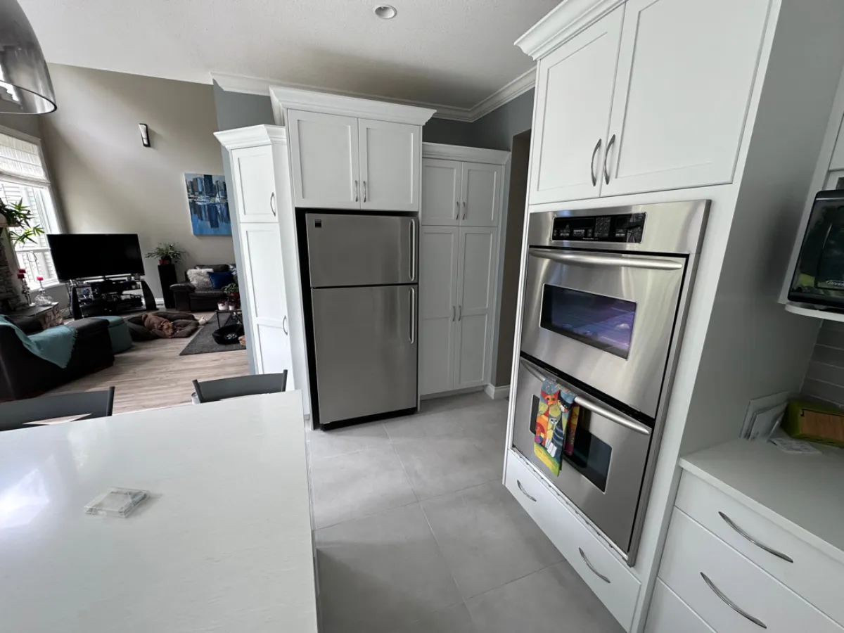 Renovated Anmore kitchen showing built-in stainless wall ovens integrated into tall white shaker cabinets