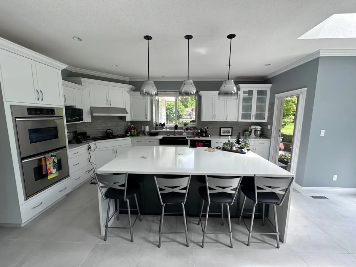Renovated Anmore kitchen with large dark island, white quartz waterfall countertop, pendant lights and bar stools