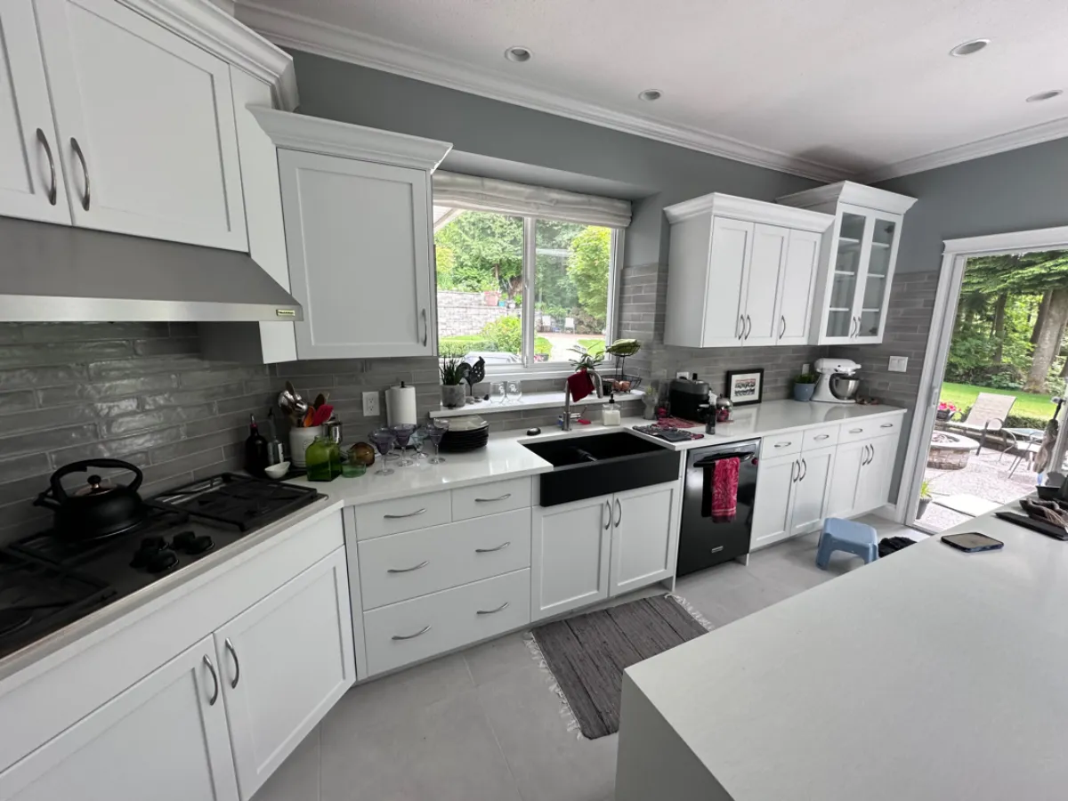 Renovated kitchen sink wall with white cabinets, black farmhouse sink and grey tile backsplash