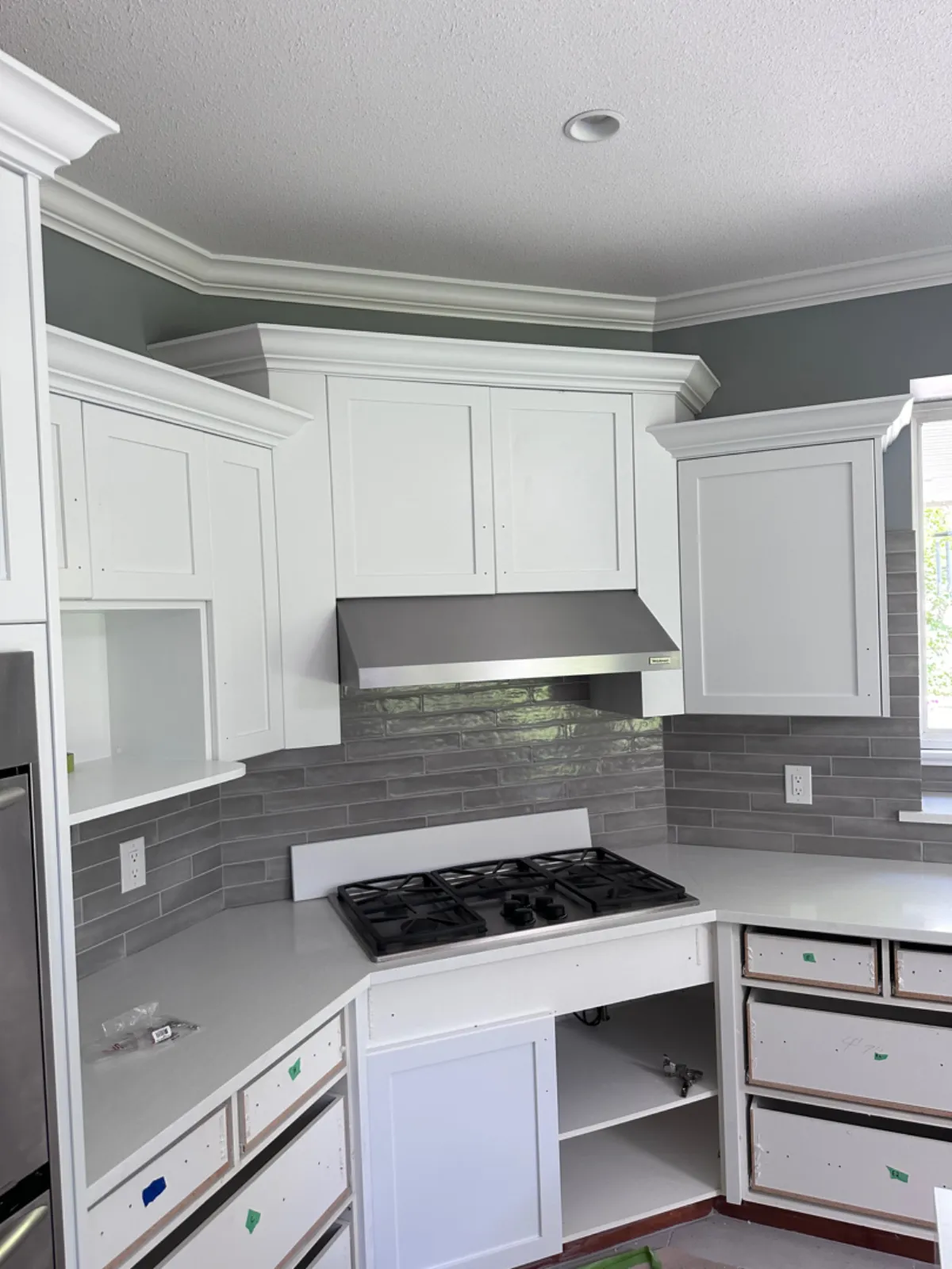 Renovated stove area with white shaker cabinets, stainless range hood and grey tile backsplash