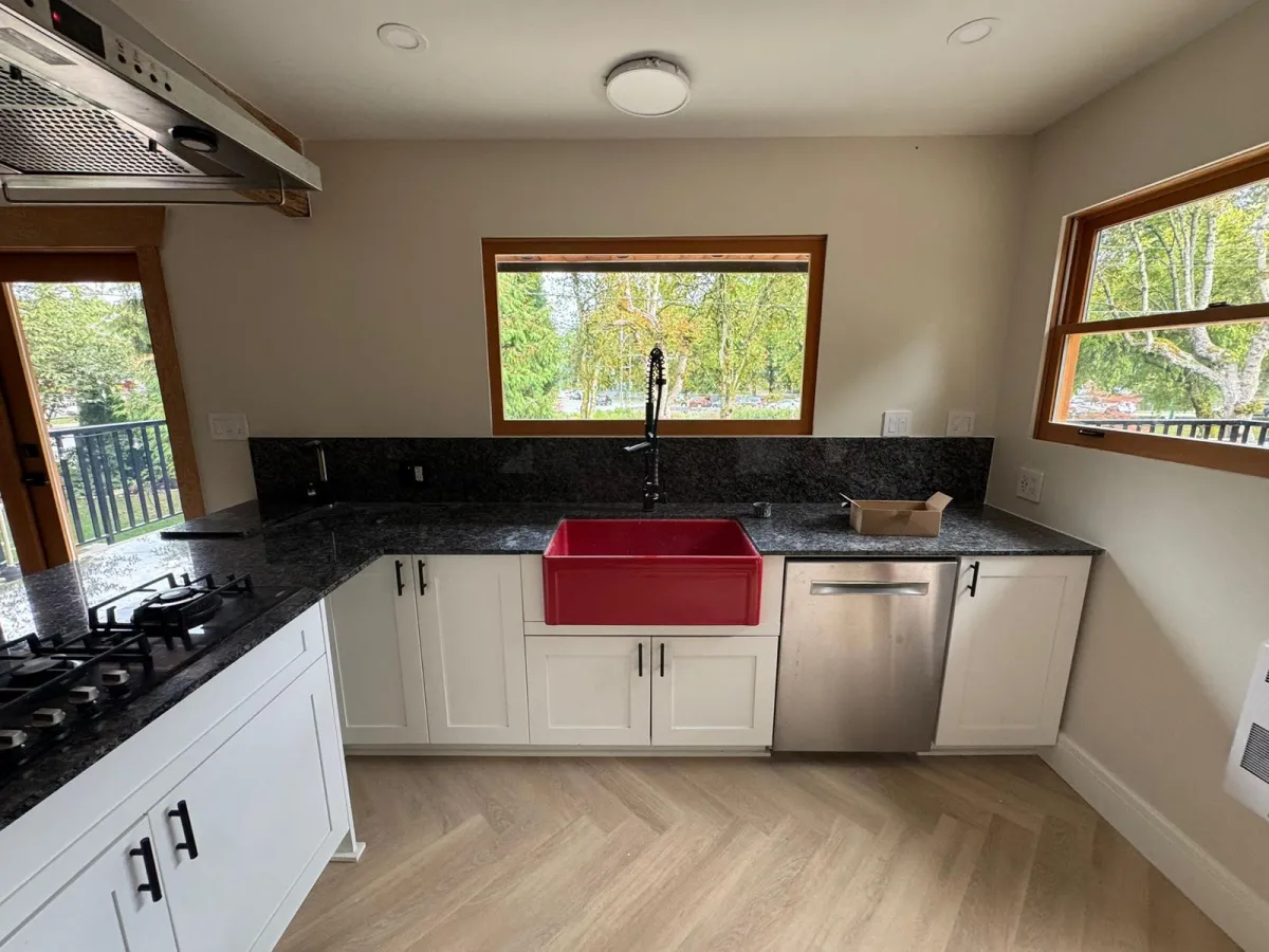Renovated kitchen with white cabinets, granite counters and red farmhouse sink