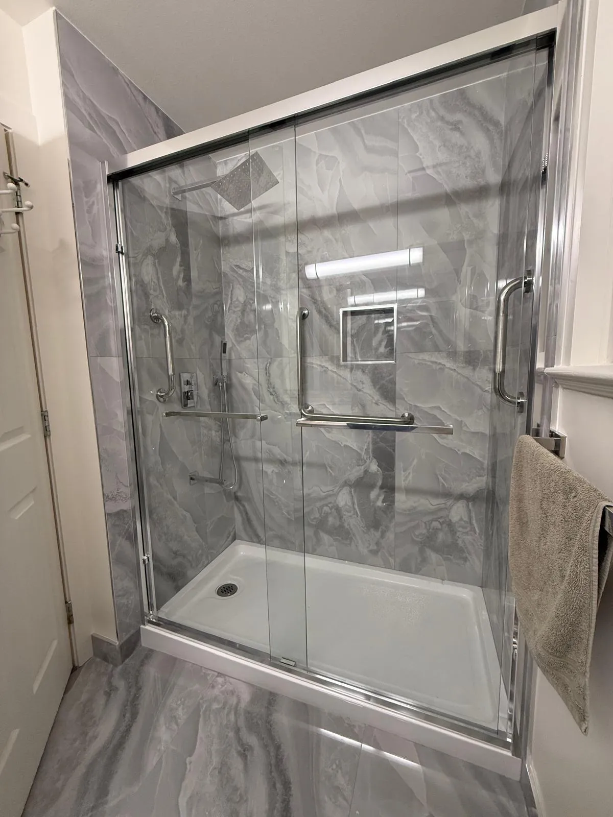 New walk-in shower with marble-look porcelain surround, glass doors and grab bars
