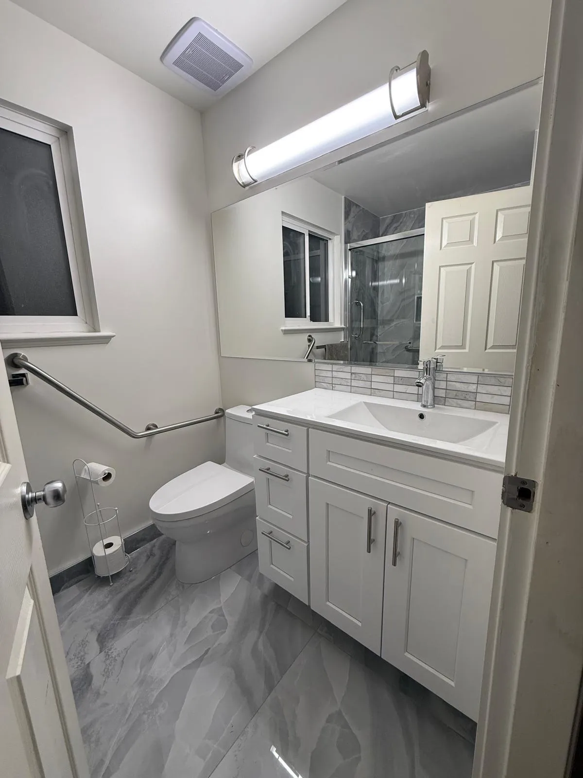 Renovated bathroom with white shaker vanity, quartz countertop, grab bars and modern lighting
