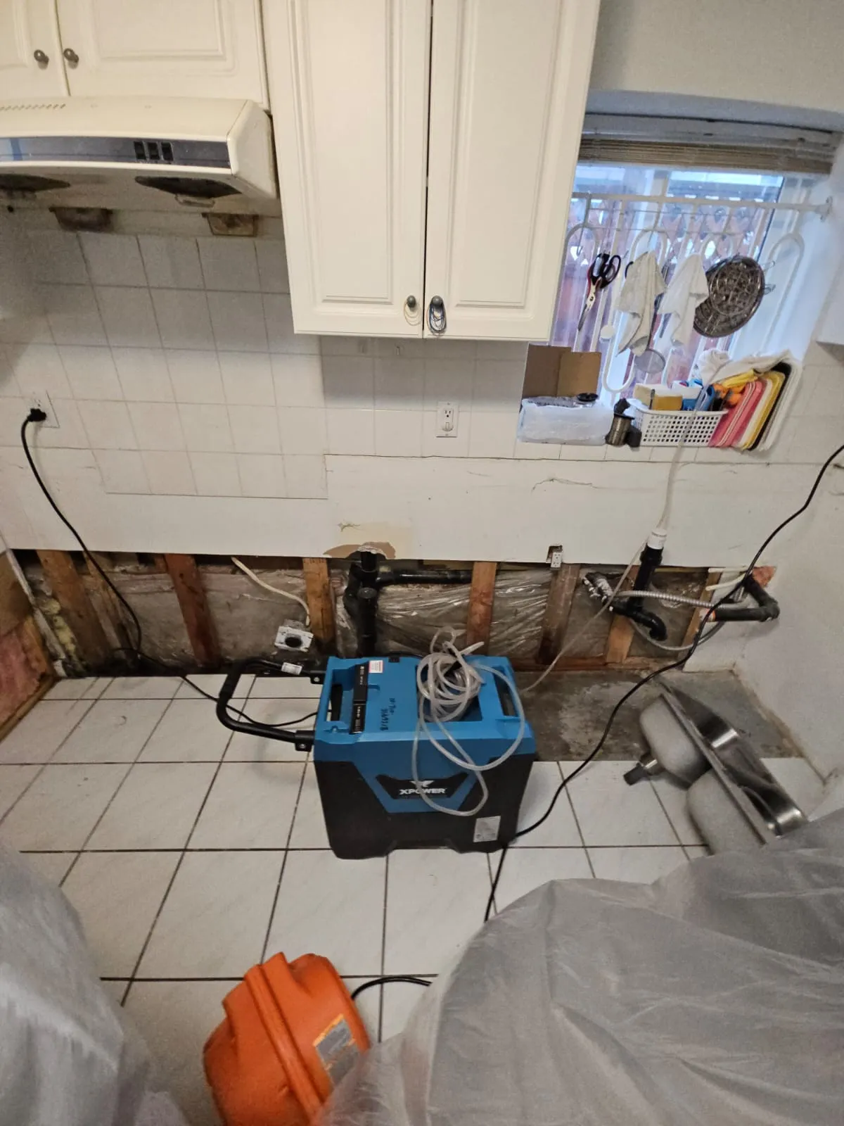 Kitchen water damage remediation with dehumidifier and exposed plumbing